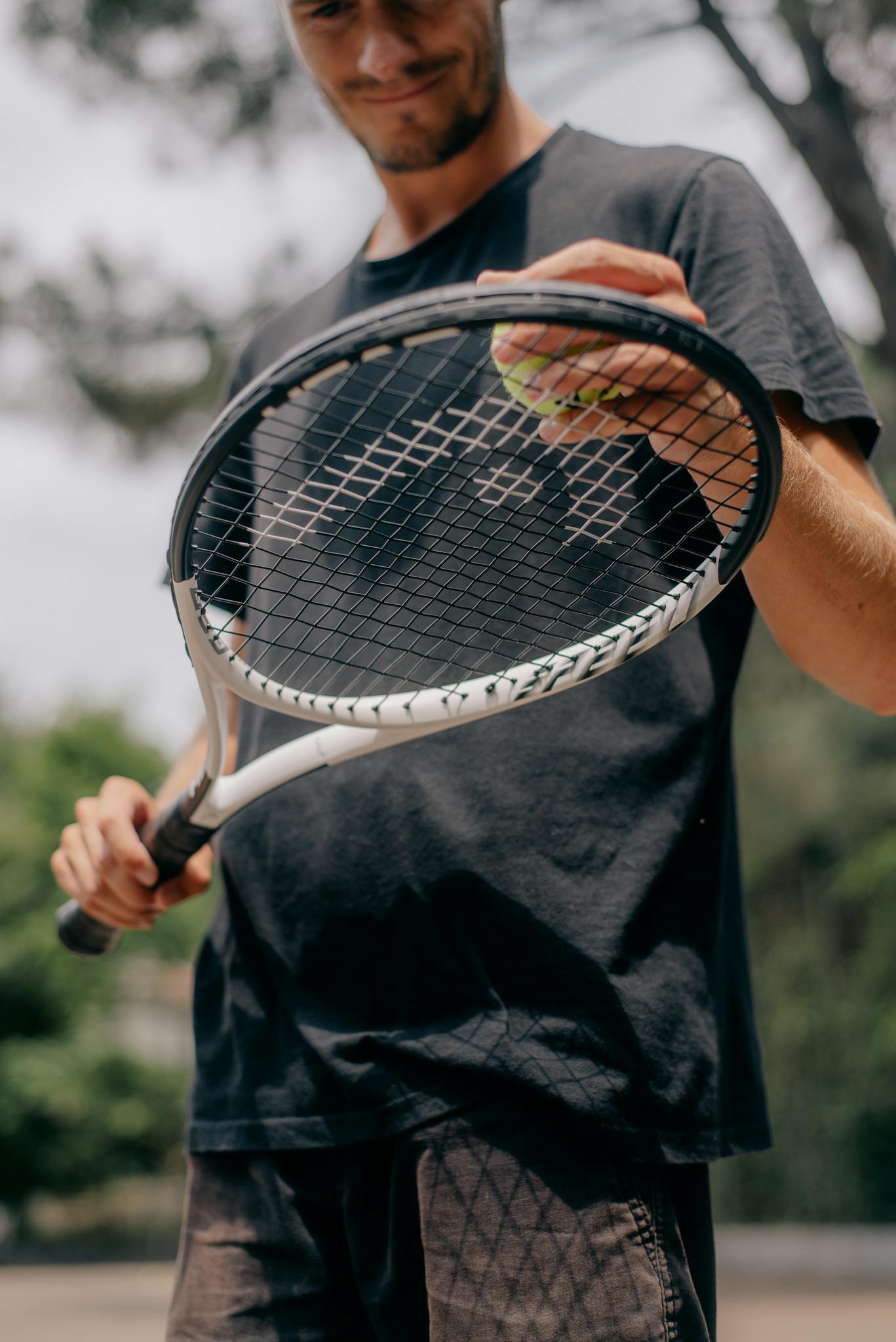 A close-up shot of a man holding a tennis racket and ball outdoors on a sunny day.