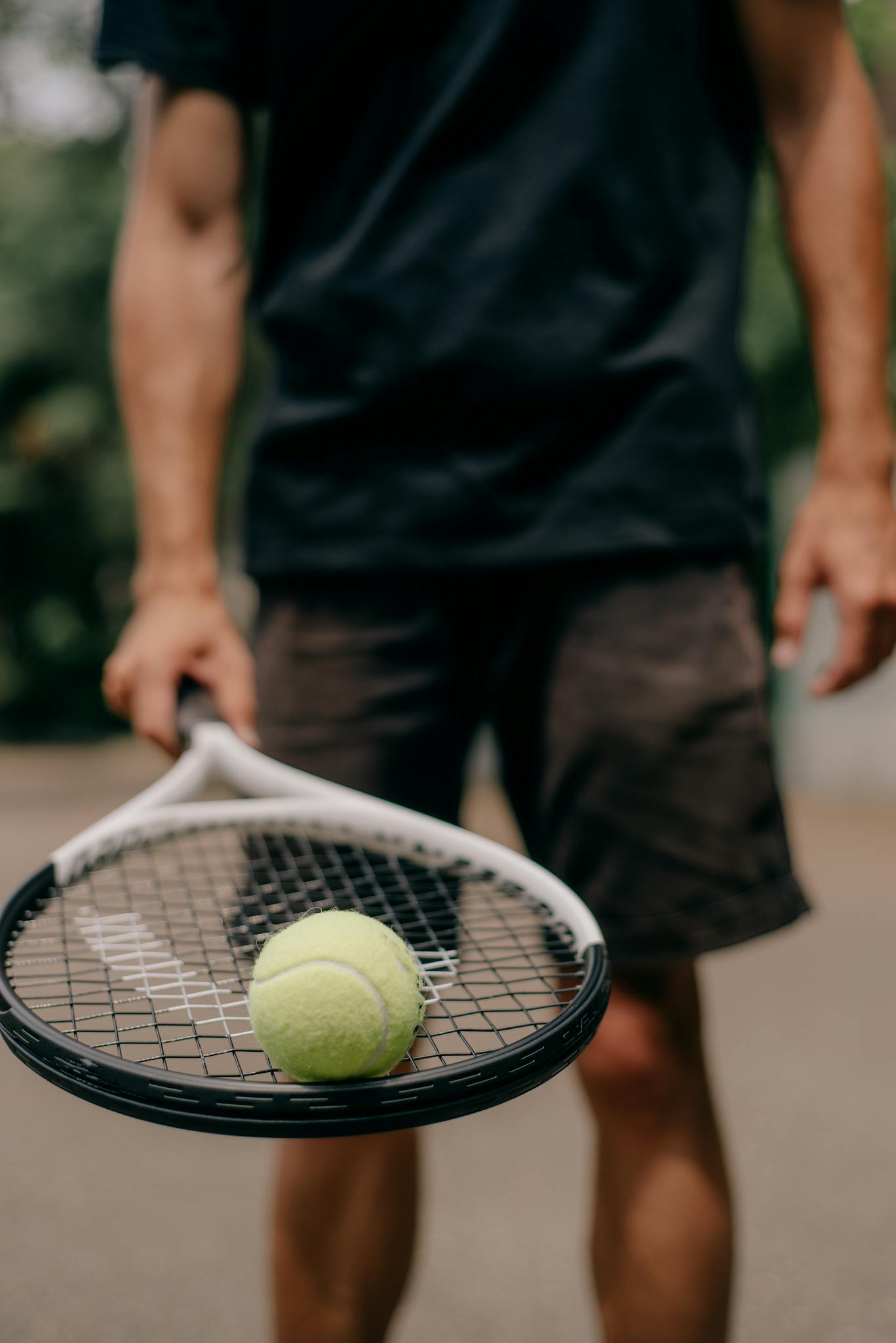 Focused shot showing a tennis racket holding a yellow tennis ball with player in background.